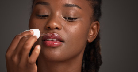 Beauty, dropper and lip serum with black woman in studio for cosmetics or dermatology routine. Hydration, mouth moisturizer and skincare with African model isolated on gray background for treatmentの写真素材