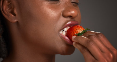Beauty, hand and strawberry with black woman in studio for organic benefits of healthy eating. Fruit, nutrition and vitamins with African model on gray background for diet, detox or weight lossの写真素材