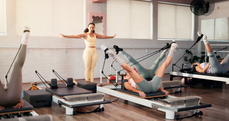 Woman, coach and pilates with stretching legs at club, reformer or motivation at exercise class. Person, talk and guide for holistic fitness, training and flexibility with resistance band at gymの写真素材