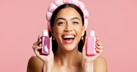 Portrait, skincare and woman with bottle in studio, beauty treatment or headband for wellness shine. Healthy glow, advertising or person with facial product for dermatology, mockup or pink backgroundの写真素材