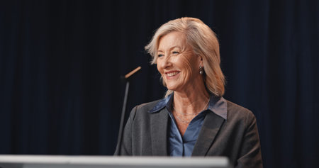 Politics, smile and speech with mature woman on stage for democracy, election or government campaign. Happy, microphone and podium with speaker at conference, meeting or summit for support or voteの写真素材