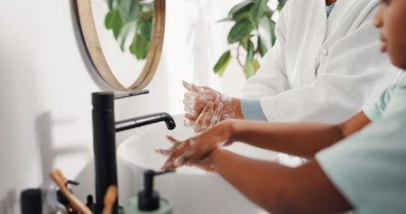 Washing hands, kid and mother in bathroom for cleaning, learning hygiene and bacteria safety. Parent, child and soap by sink in home for germ prevention, health and foam for teaching disinfectionの写真素材