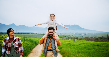 Portrait, grass field or parents with child for bonding, love or connection for weekend vacation. Countryside holiday, happy people or carry girl on shoulders for outdoor fun, space or relationshipの写真素材