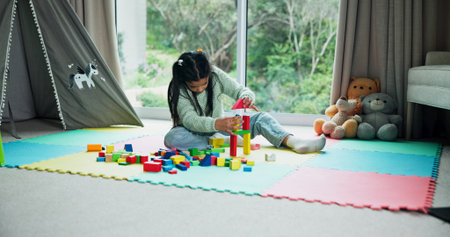 Building blocks, relax and game with kid in home for learning, creative puzzle and growth. Child development, problem solving and wooden toys with girl in playroom of house for solution and shapesの写真素材