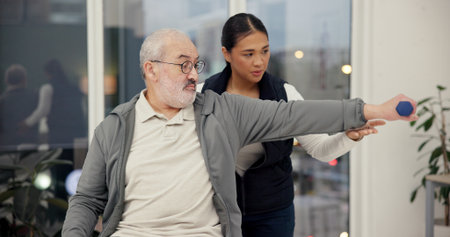 Dumbbell, physiotherapist and exercise with senior man in rehabilitation, help or muscle recovery. Physical therapy, woman and elderly patient weightlifting, fitness and health in medical clinicの写真素材