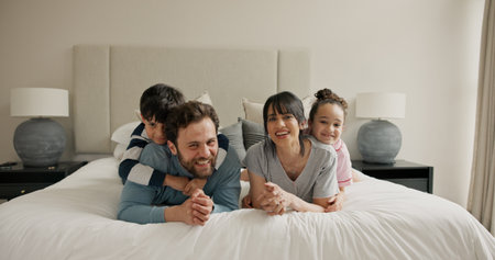 Parents, children and portrait on bed with play, smile and bonding for love with pyjamas at house. People, mom and dad with kids, happy or relax in morning, care and laugh at family home in Spainの写真素材