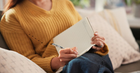 Woman, hands and writing on sofa with journal for planning goals, creative idea or process emotions. Daily reflection, notes or person in home with diary for self improvement, inspiration or insight.の写真素材