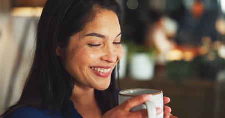 Coffee, smile and businesswoman in office at night for calm, relax or energy at company. Drinking, cappuccino and professional female person with mug for warm beverage with peace in workplace.の写真素材