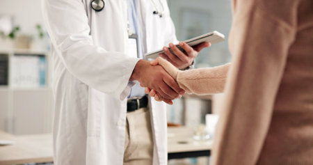 Doctor, patient or handshake in office with tablet for healthcare assessment, welcome or appointment. Medical professional, people and shaking hands with tech for consultation, greeting or thank you.の写真素材