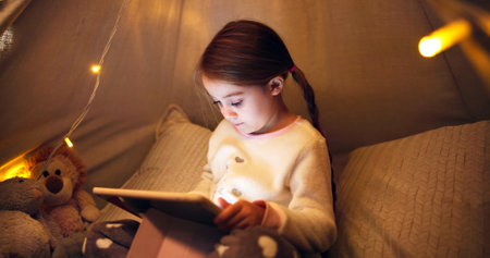 Night, child and relax with tablet in bedroom for ebook, reading fantasy and bedtime story. Late, girl and scroll with digital tech in home for online fairytale, kids storytelling app and literature.の写真素材
