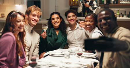 Friends, selfie and happy with dinner at restaurant, hug and drinks at reunion with post on social media. People, smile and excited at party, embrace or photography for memory with group at dinerの写真素材