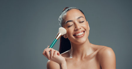 Makeup, brush and and woman in studio for cosmetics, contouring and beauty treatment. Happy, blush and female person with tool for blending, application and cosmetology routine by gray background.の写真素材