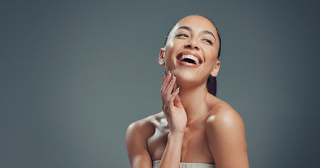 Laughing, skincare and hands with woman in studio for beauty, self care and clear skin. Glow, dermatology and hydration with female person on gray background space for shine, aesthetic and mockupの写真素材