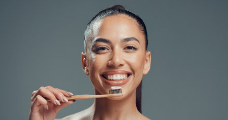 Dental health, portrait and woman with bamboo toothbrush for oral wellness, fresh breath and smile. Toothpaste, clean teeth and face of person with eco friendly tool in studio on gray backgroundの写真素材