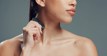 Skincare, neck or woman in studio with gua sha, facial benefits or massage in self care. Cosmetology, body tone and girl on gray background with tool, sculpting or lymphatic drainage for firm skin.の写真素材