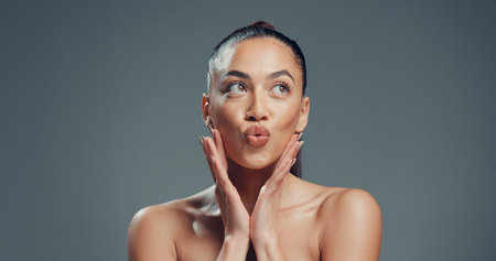 Hands, skincare and pout with woman in studio for beauty, self care and clear skin. Glow, dermatology and hydration with female person on gray background space for shine, aesthetic and collagenの写真素材