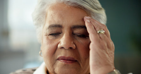 Senior woman, headache and stress in home with vertigo, hypertension and symptoms in lounge for retirement. Elderly person, frustrated and migraine with pain, burnout or fatigue in morning at houseの写真素材