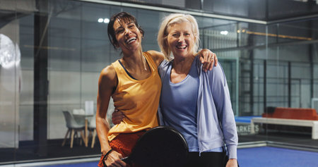 Padel, sports and portrait of women hug for game, match and training for challenge. Indoor court, happy and mature people with racket for workout, exercise and fitness for practice and hobbyの写真素材