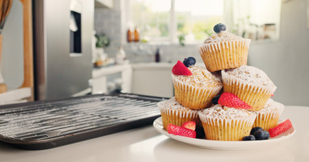 Cupcakes, kitchen and baking with fruit for sweet dessert, recipe or pastry creation in home. Empty, baked and muffin with icing sugar, strawberries or blueberries for treat or cake serving on plateの写真素材