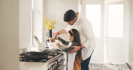 Baking, ladle or teaching with father and daughter in kitchen of home for bonding or development. Bowl, cooking or learning with girl child and single parent man in apartment for recipe instructionsの写真素材
