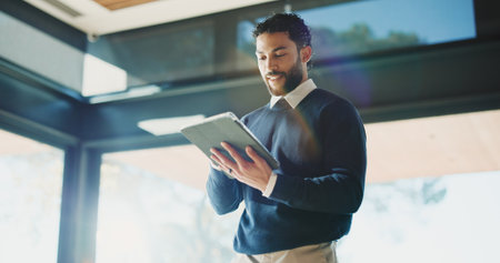 Man, realtor and tablet in office for reading, property management and service review. Low angle, estate agent and digital tech in agency for commission update, scroll and smile for reflectionの写真素材
