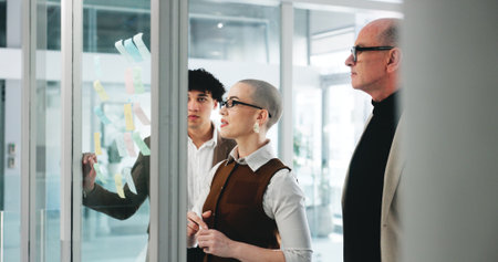 Collaboration, glass wall and planning with business people in office together for project management. Brainstorming, sticky notes and teamwork with employee group in corporate workplace for meetingの写真素材