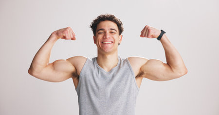 Portrait, man and flex bicep for fitness, strength and workout progress in studio. Smile, person and bodybuilder show muscle for growth, strong or confident with exercise results on white backgroundの写真素材