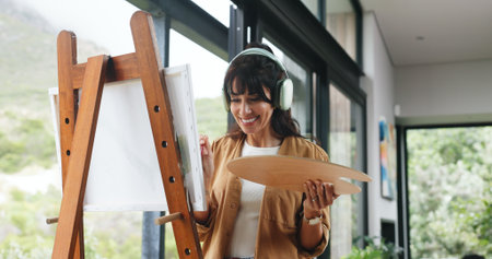 Painter, home or headphones with canvas for creativity project, self expression or happiness for craft. Tech, streaming music or mature woman with palette for artistic activity, creation or low angleの写真素材