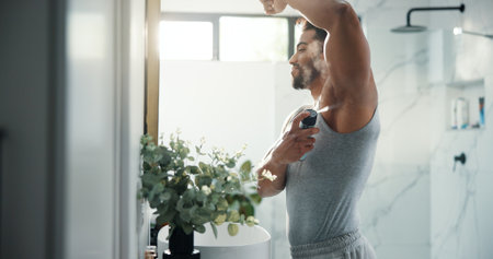 Man, hygiene and spray armpit at bathroom mirror, home and smile for deodorant with flare in morning. Person, grooming and self care with fragrance for odor, sweat or happy with bottle at apartmentの写真素材