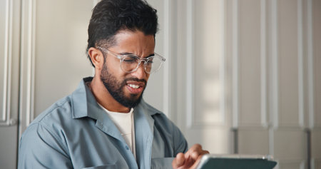 Confused, reading and man with tablet in home with notification, networking or social media. Doubt, error and male person with digital technology for spam text or subscription cancellation in house.の写真素材