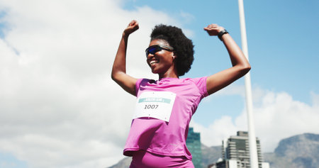 Black woman, marathon and celebration with winning at finish line with low angle, goals and performance. Person, champion and happy runner with achievement, success and fist pump for sports milestoneの写真素材