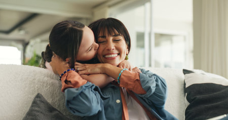 Kiss, hug and mother with child on sofa in home with love, support and care in living room. Smile, comfort and kid embracing mom for bonding together at house with connection, relax or family time.の写真素材