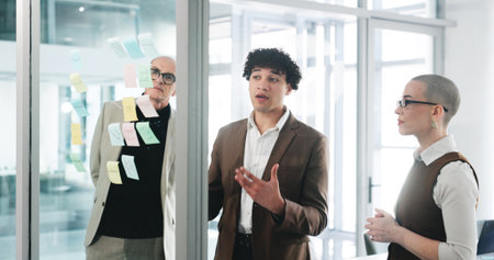 Conversation, glass wall and planning with business people in office together for project management. Collaboration, brainstorming and sticky notes with corporate employee team at work for meetingの写真素材