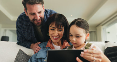Tablet, relax and parents with child on sofa in home for playing educational video game on app. Happy, digital technology and girl kid with mom and dad for watching movie in living room at house.の写真素材