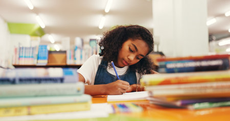 Writing, homework and girl in library, kid and education with knowledge, learning and growth. Student, notebook and child development with assessment, creativity and inspiration for project and ideasの写真素材