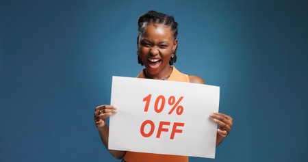 Happy, black woman or sign with discount for advertising or marketing on a blue studio background. Female person, promoter or model with poster or billboard for shopping deal, percentage or low priceの写真素材