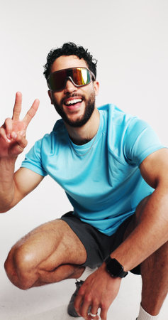 Studio, athlete and man with sport sunglasses, peace sign and happiness for UV protection spectacles. White background, glare reduction and person with smile for eyewear, eye care and visual shieldの写真素材