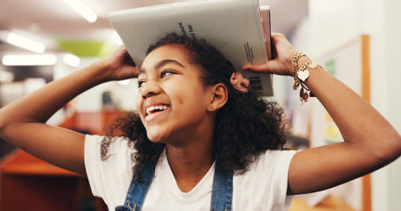 Smile, child and student with books in library for learning, story time and literature education. Happy, kid and walk with novel for studying, language development and scholarship of knowledge growthの写真素材