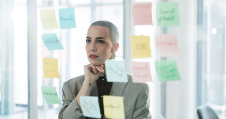 Glass wall, planning and thinking with business woman in office for brainstorming or strategy. Mind map, solution and sticky notes with corporate employee in workplace for project managementの写真素材