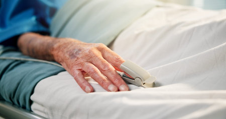 Hands, old person and rest with oximeter in hospital bed to monitor pulse, blood levels and post...