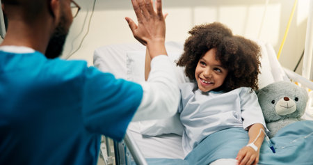 Boy, doctor and high five with smile in hospital bed, happy and care with support for recovery. Pediatrician, child and excited with teddy bear, motivation and celebration with healing at clinicの写真素材