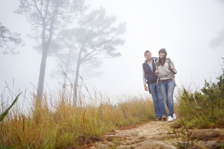 Below, couple and hiking in forest for fitness adventure, morning fog and trekking on holiday. Portrait, people and backpacking journey on trail with mist, explore nature and bonding together on tripの写真素材