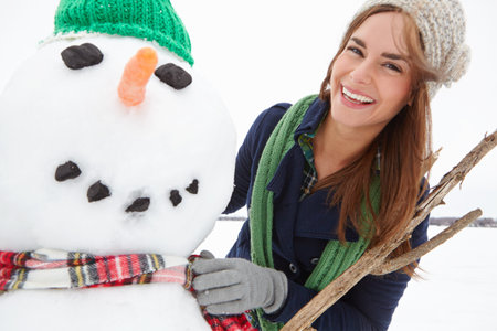Winter, woman and portrait with snowman outdoor for holiday tradition, travel adventure and activity. Cold, tourist and happy with snow figure in countryside for festive season and tourism experienceの写真素材