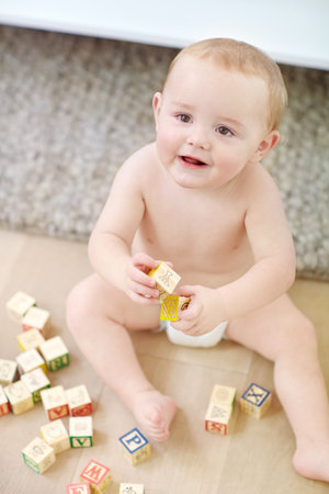 Happy boy, playful toddler and floor with wooden blocks for childhood development or learning in home. Youth, child or kid playing with toys for fine motor skills, coordination or building in houseの写真素材