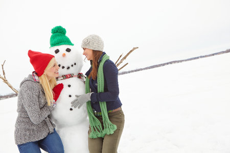 People, friends and laugh with snowman outdoor for Christmas, snow activity and bonding on holiday. Smile, women and embrace with frosty sculpture of winter fun, funny ice character and xmas vacationの写真素材
