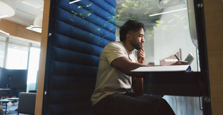 Creative, man and laptop with writing in booth with notes, and privacy for feedback. Soundproof, cubicle and person with proposal for ad campaign, digital marketing or research in podの写真素材