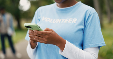 Hands, phone and volunteer with woman outdoor for charity, community outreach or food drive. App, text message and typing with person in park for activism, ngo donation or non profit communicationの写真素材