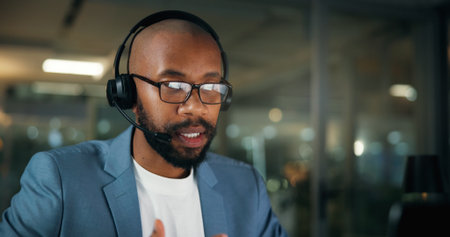 Call center, consultant and business black man in office for security, emergency hotline and night. Virtual advisor, dispatch operator and alarm verification specialist with person and overtimeの写真素材