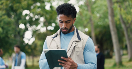 Agenda, tablet and volunteer with man in park for charity, community outreach or food drive. App, research and schedule with serious person outdoor in nature for activism, ngo or non profit donationの写真素材