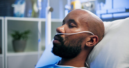 Man, breathing tubes or sleeping on hospital bed for post surgery, healthcare or recovery. Sick patient, black person or rest with nasal cannula in ICU for respiratory support, ventilation or healingの写真素材